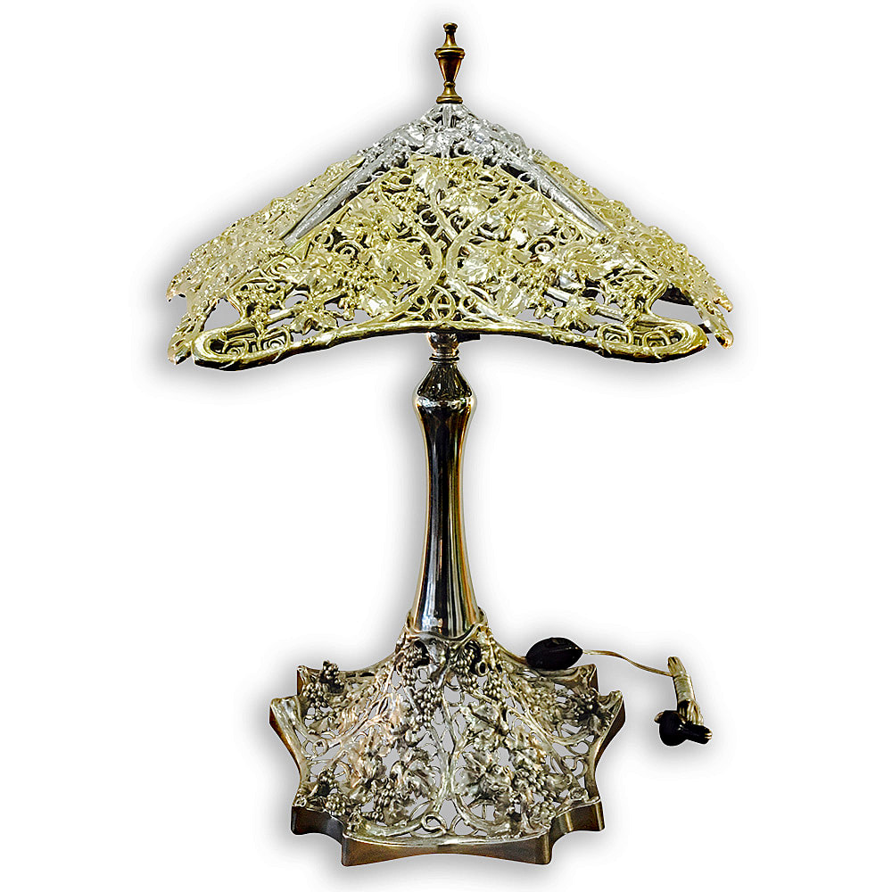 This ornate antique table lamp has been meticulously restored by Chelsea Plating Company to its former elegance. The base, nickel-plated with careful precision, complements the open work shade that has been plated in 24k gold. The harmonious blend of nickel and gold captures the refined artistry of a past era, transformed through skilled restoration into a timeless piece of decorative beauty.